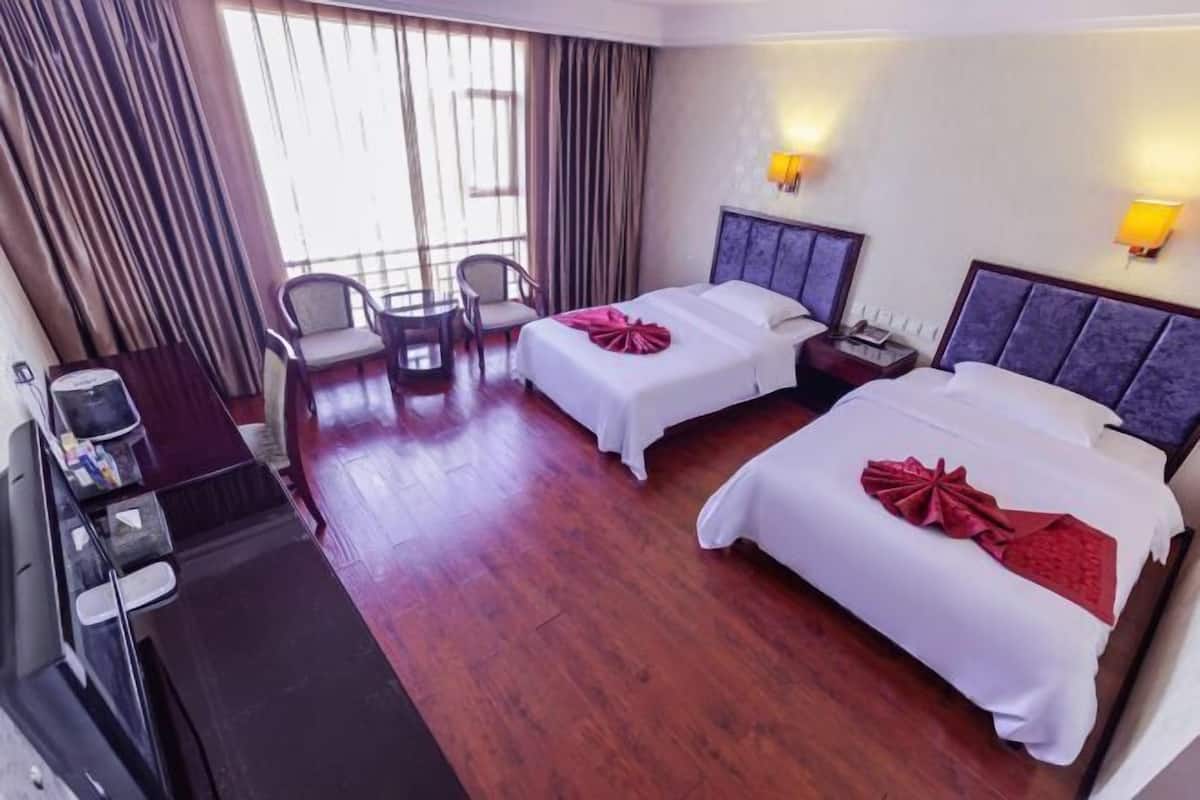 A hotel room with two beds, a desk, chairs, and a large window with curtains.