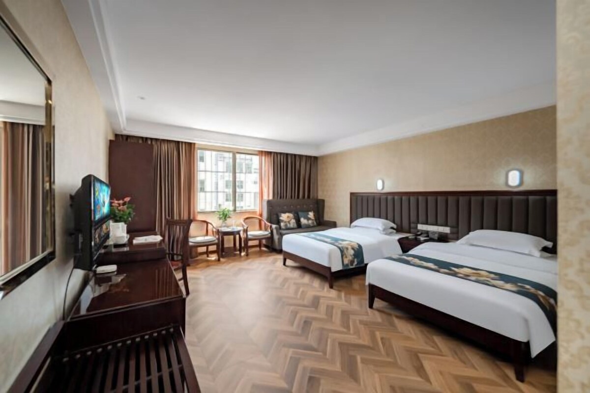 A hotel room with two beds, a desk, a chair, a television, and a window.