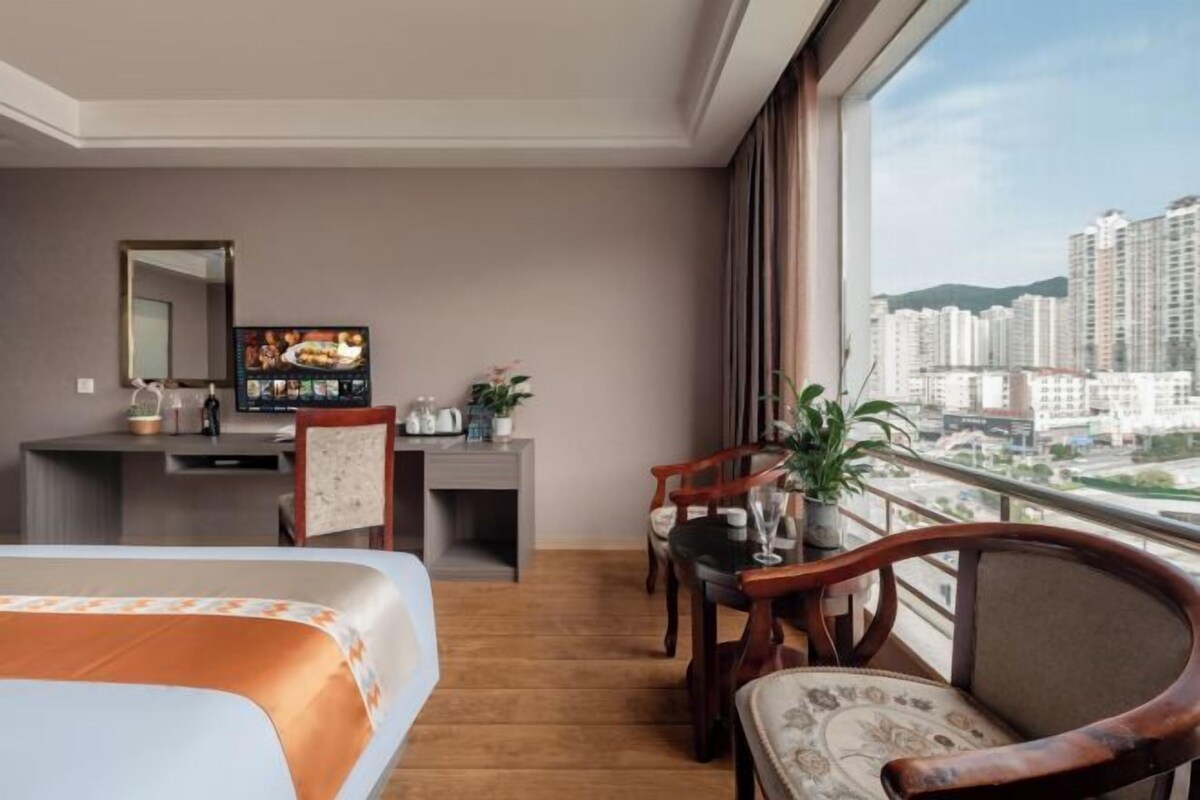 A hotel room with a bed, a desk, a chair, a TV, and a balcony with a city view.
