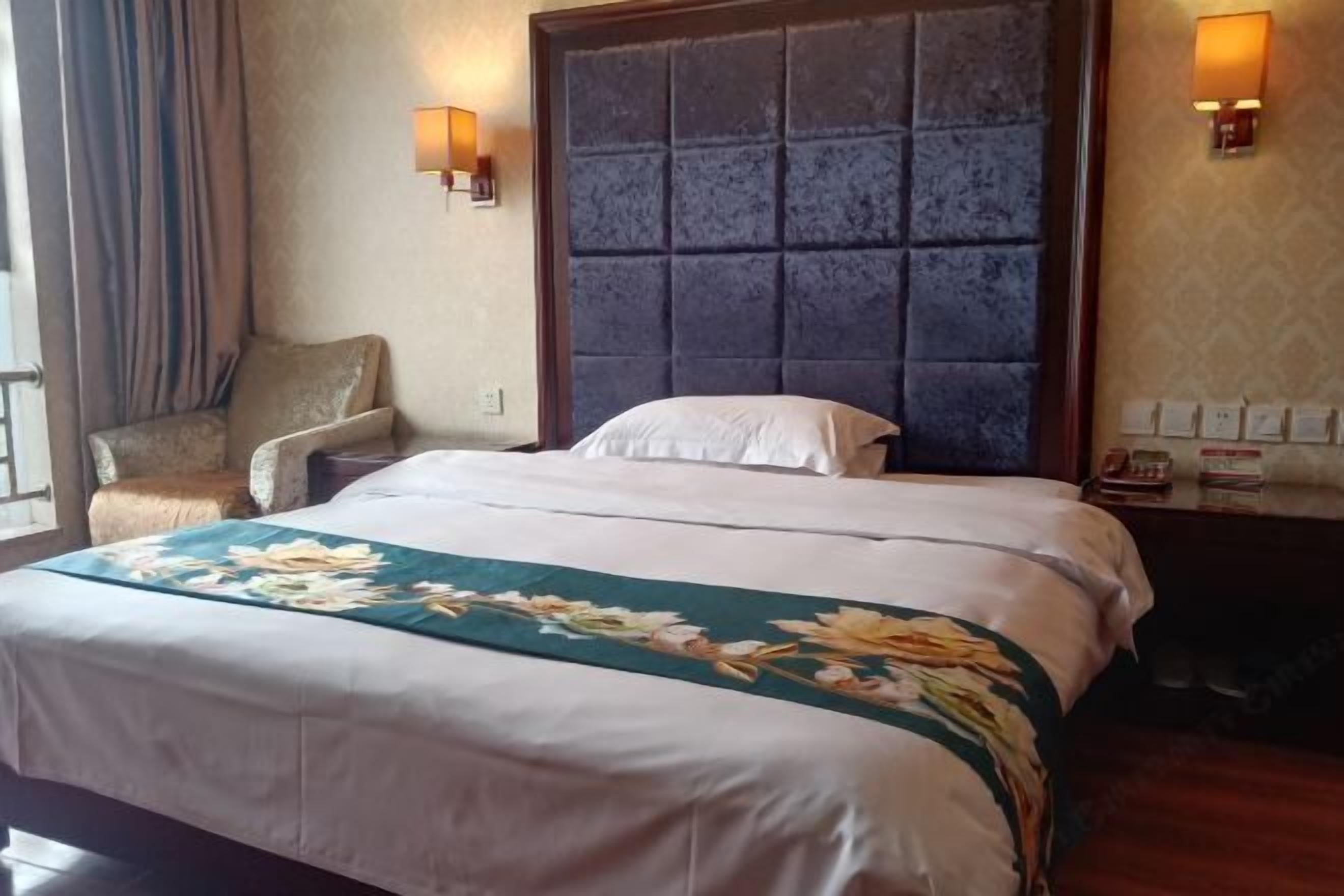 Une chambre d’hôtel avec un grand lit, une chaise, deux appliques murales et une table de chevet avec une lampe.
