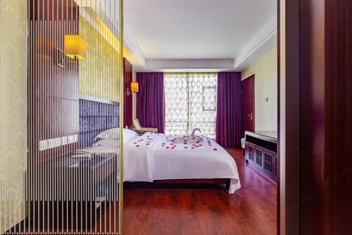 A hotel room with a bed, a desk, a chair, a TV, and a window with curtains.