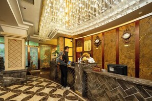 Un hall d’hôtel avec un sol en marbre, un comptoir d’accueil et un lustre.
