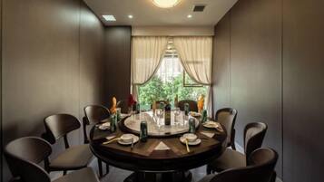A round dining table with chairs, a chandelier, and a view of greenery through the window.