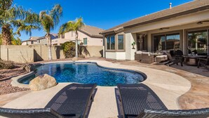 A backyard with a swimming pool, lounge chairs, and a patio area. - Hole in One with pool and putting green! (Goodyear)
