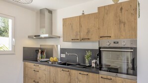 Uma cozinha moderna com armários de madeira, exaustor de aço inoxidável, forno embutido e uma janela que oferece luz natural.