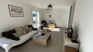 Uma sala de estar com sofá, mesa de centro, rack para TV e um quadro na parede.