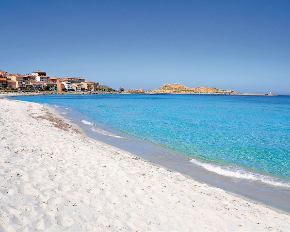 A beach with clear blue water, sandy shore, and buildings in the background. - NEW HOUSE MONTICELLO 6 PERSONS (MONTICELLO)