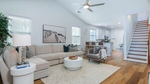 Ein geräumiges Wohnzimmer mit einem beigefarbenen Sofa, einem weißen Couchtisch und einem modernen Deckenventilator.