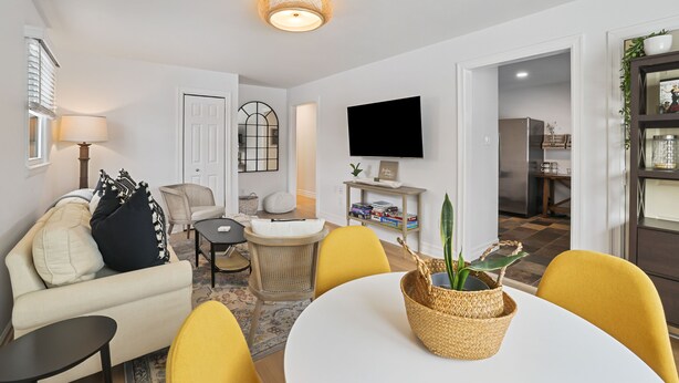 A modern living room with a sofa, yellow chairs, a dining table, and a TV mounted on the wall. - Leesburg Hideaway- King Bed + Private Backyard (Leesburg)
