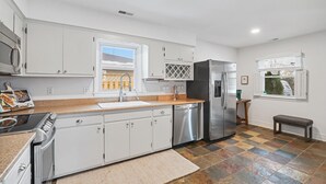 A modern kitchen with white cabinets, stainless steel appliances, a granite countertop, and a patterned rug. - Leesburg Hideaway- King Bed + Private Backyard (Leesburg)