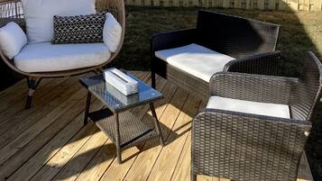 A wooden deck with wicker furniture, including a chair and a sofa, and a small table.
