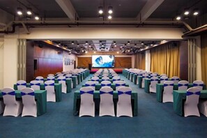 A conference room with rows of tables and chairs, a large screen at the front, and a blue carpeted floor. - Shile Hotel (Zhongshan Station) (Zhongshan)