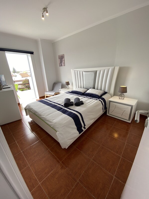 A bedroom with a large bed, a nightstand, a lamp, and a view of the outside.