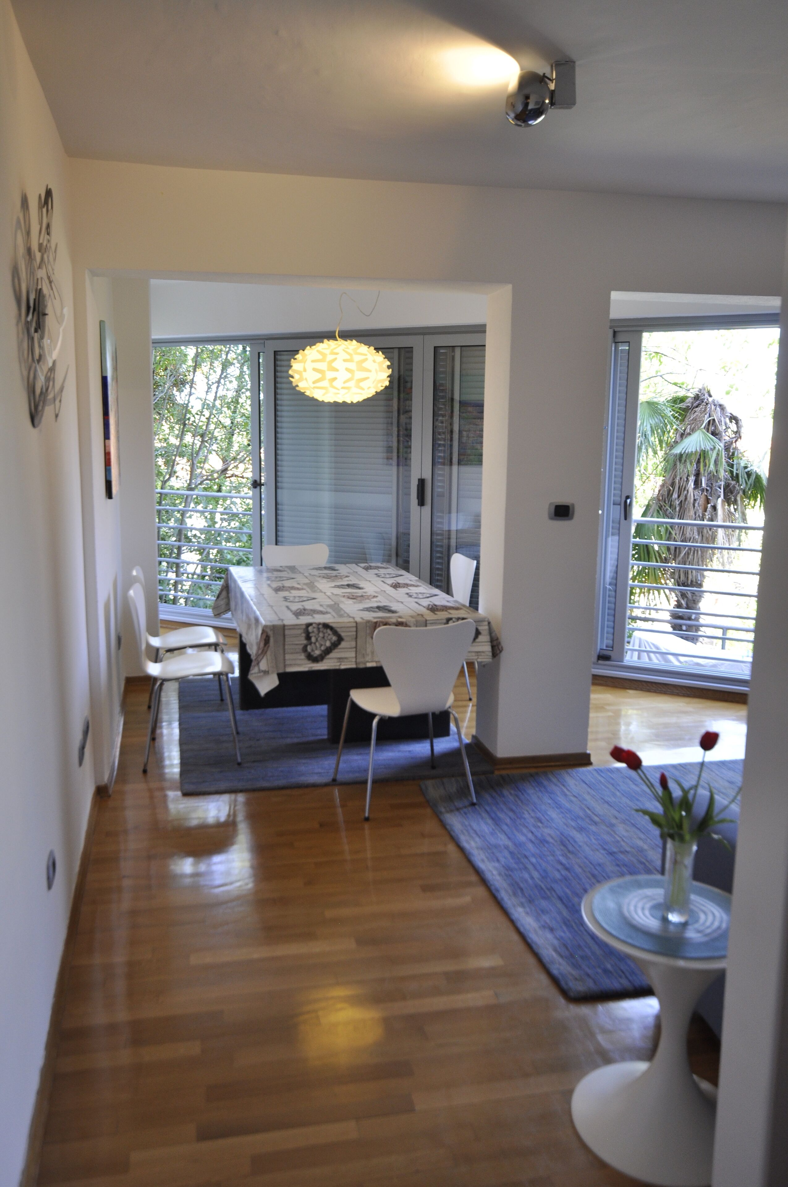 A dining area with a table and chairs, a hanging light fixture, and a view of the outdoors through a glass door.