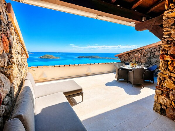A balcony with a stone wall, a table with chairs, and a view of the sea.