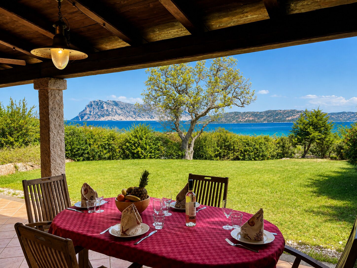 An outdoor dining area with a table set for four, overlooking a scenic view of the sea and mountains.