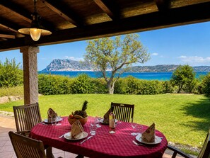 Un espacio de comedor al aire libre con una mesa preparada para cuatro personas, con vistas panorámicas al mar y las montañas.