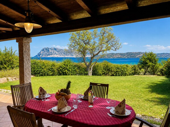 Un espacio de comedor al aire libre con una mesa preparada para cuatro personas, con vistas panorámicas al mar y las montañas.