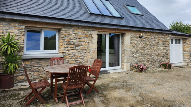 Une maison en pierre avec un toit en tuiles, une terrasse avec une table et des chaises, et une plante en pot.
