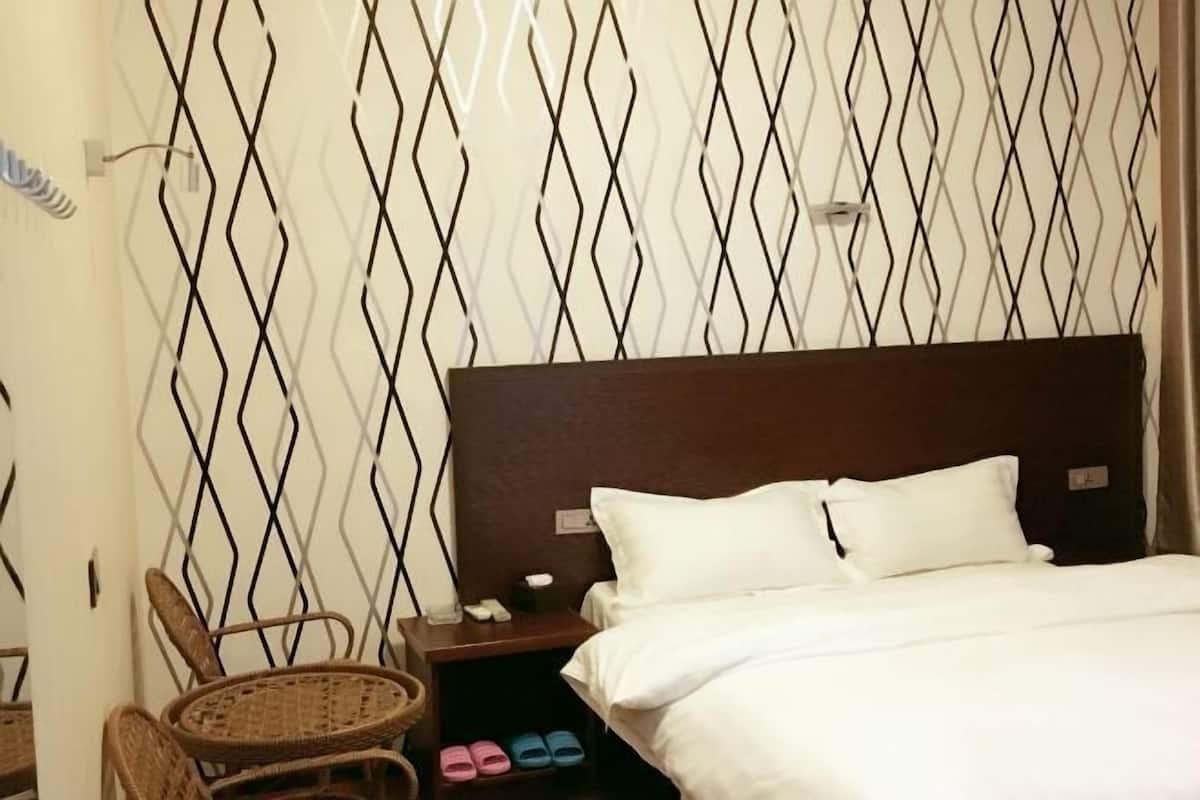 Una habitación de hotel con cama, mesita de noche, una silla de mimbre y un zapatero.