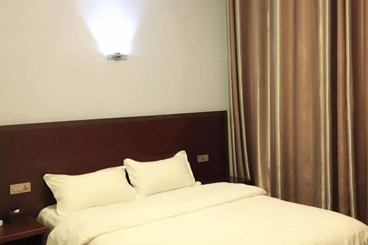 Una habitación de hotel con cama, mesita de noche, lámpara de pared y cortina.