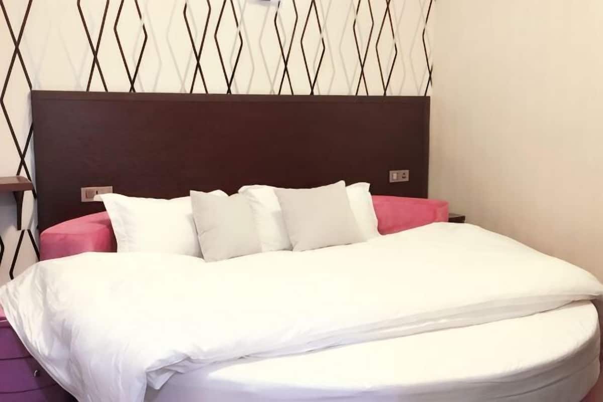 Una cama con ropa de cama blanca, cabecera oscura y pared con un diseño geométrico.