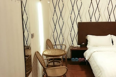 A hotel room with a bed, a nightstand, a small table with chairs, and a patterned wall.. Shiquan Shimei Hotel