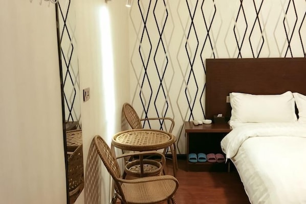 A hotel room with a bed, a nightstand, a small table with chairs, and a patterned wall. - Shiquan Shimei Hotel (Pingtang)