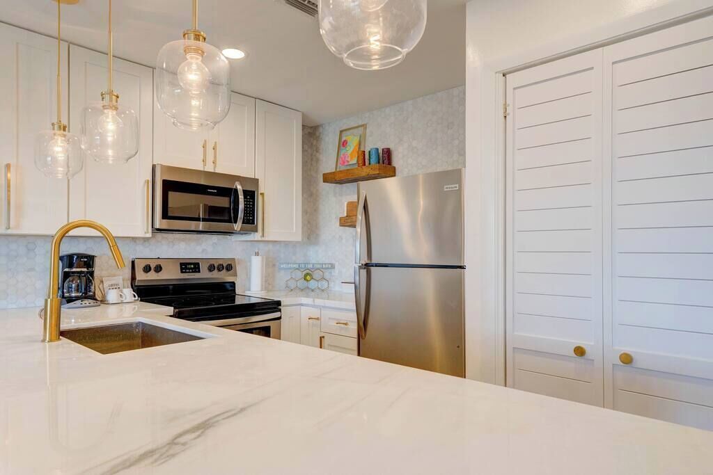 A modern kitchen with white cabinets, stainless steel appliances, and a marble countertop.