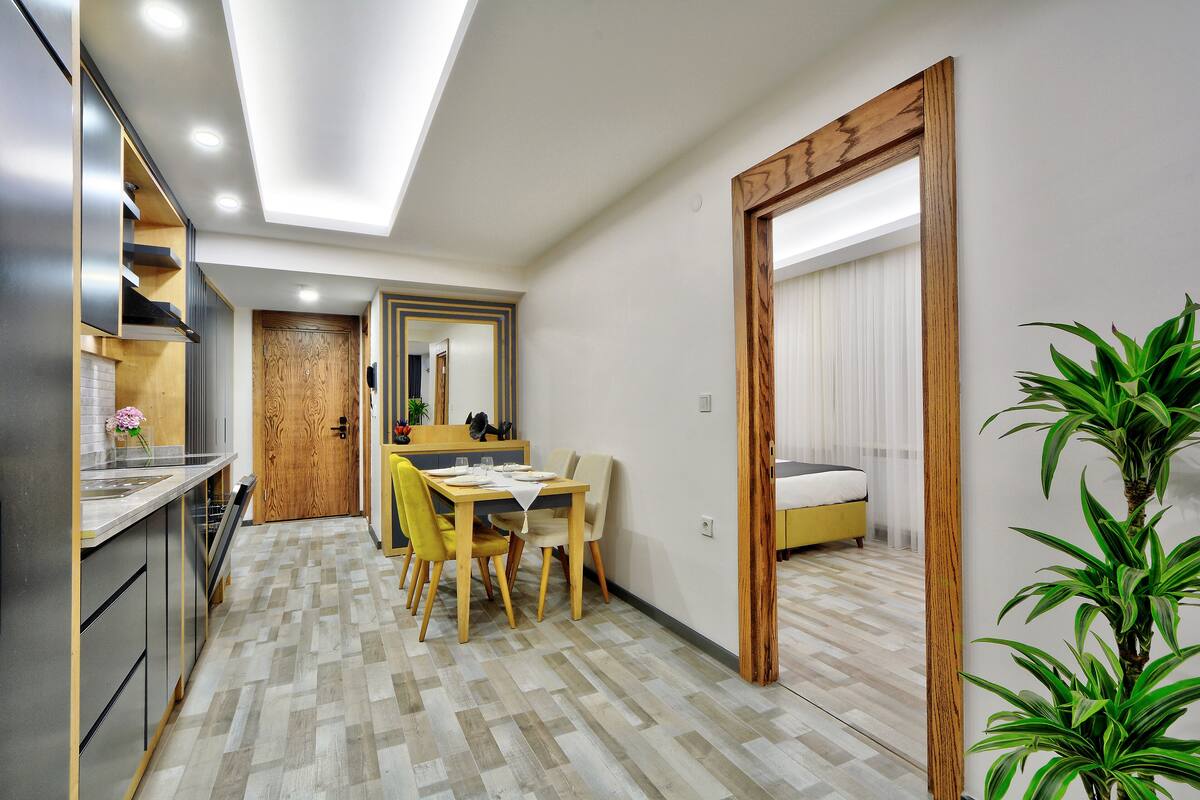 Una cocina compacta con electrodomésticos modernos, un comedor con mesa y sillas de madera, y un dormitorio con cama y un espejo grande.