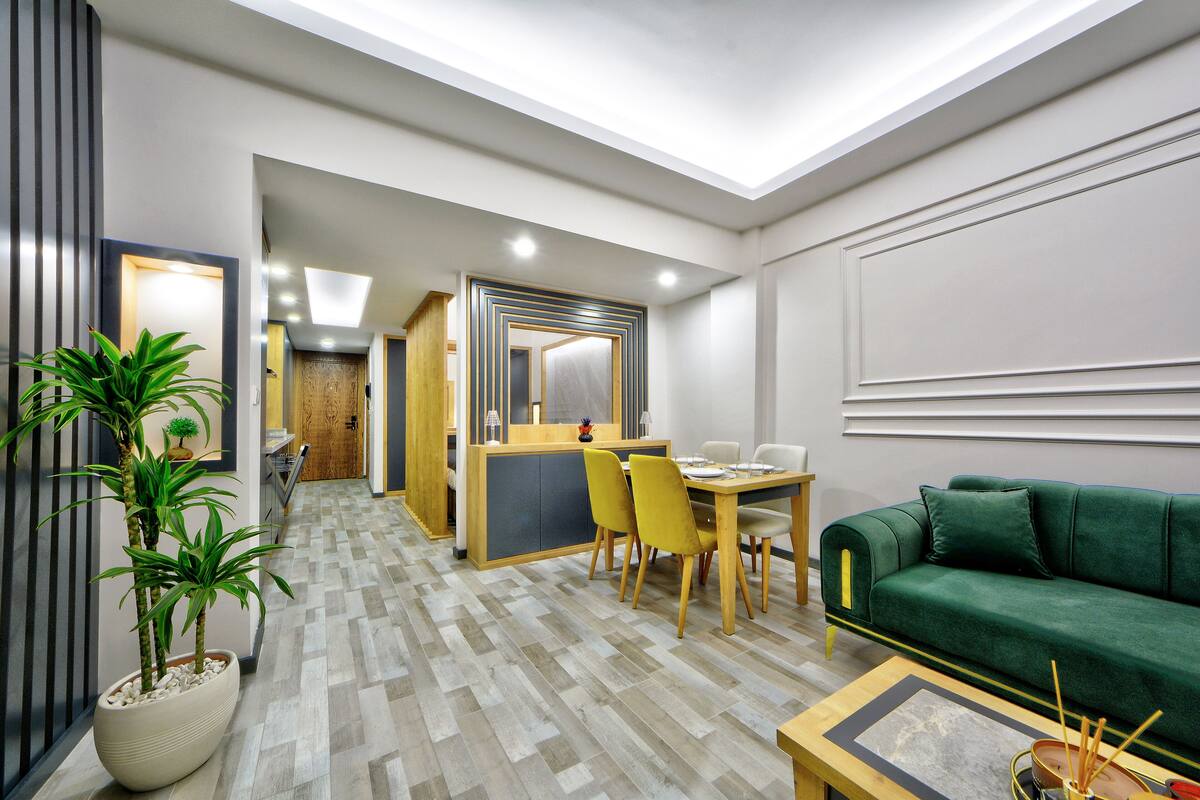Una sala de estar moderna con un sofá verde, una mesa de comedor con sillas y una planta en maceta.