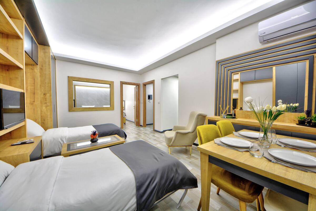 Una habitación de hotel con dos camas, una mesa de comedor con sillas, un televisor y un equipo de aire acondicionado.