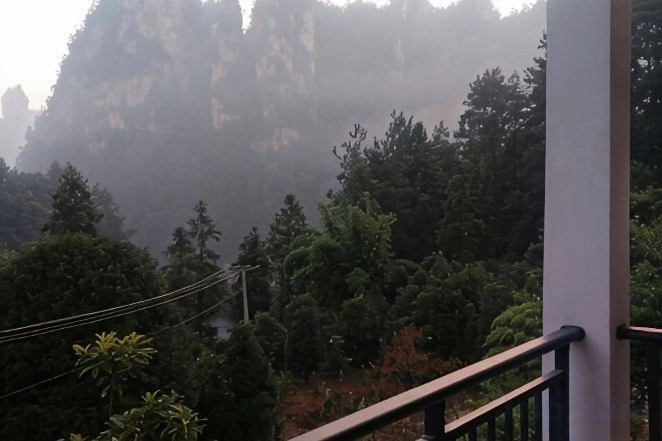 A mountainous landscape with dense forest and a building with a balcony.