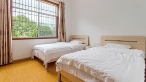 Una habitación con dos camas individuales, un ventanal con cortinas y suelo de madera.