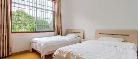 Una habitación con dos camas individuales, un ventanal con cortinas y suelo de madera.