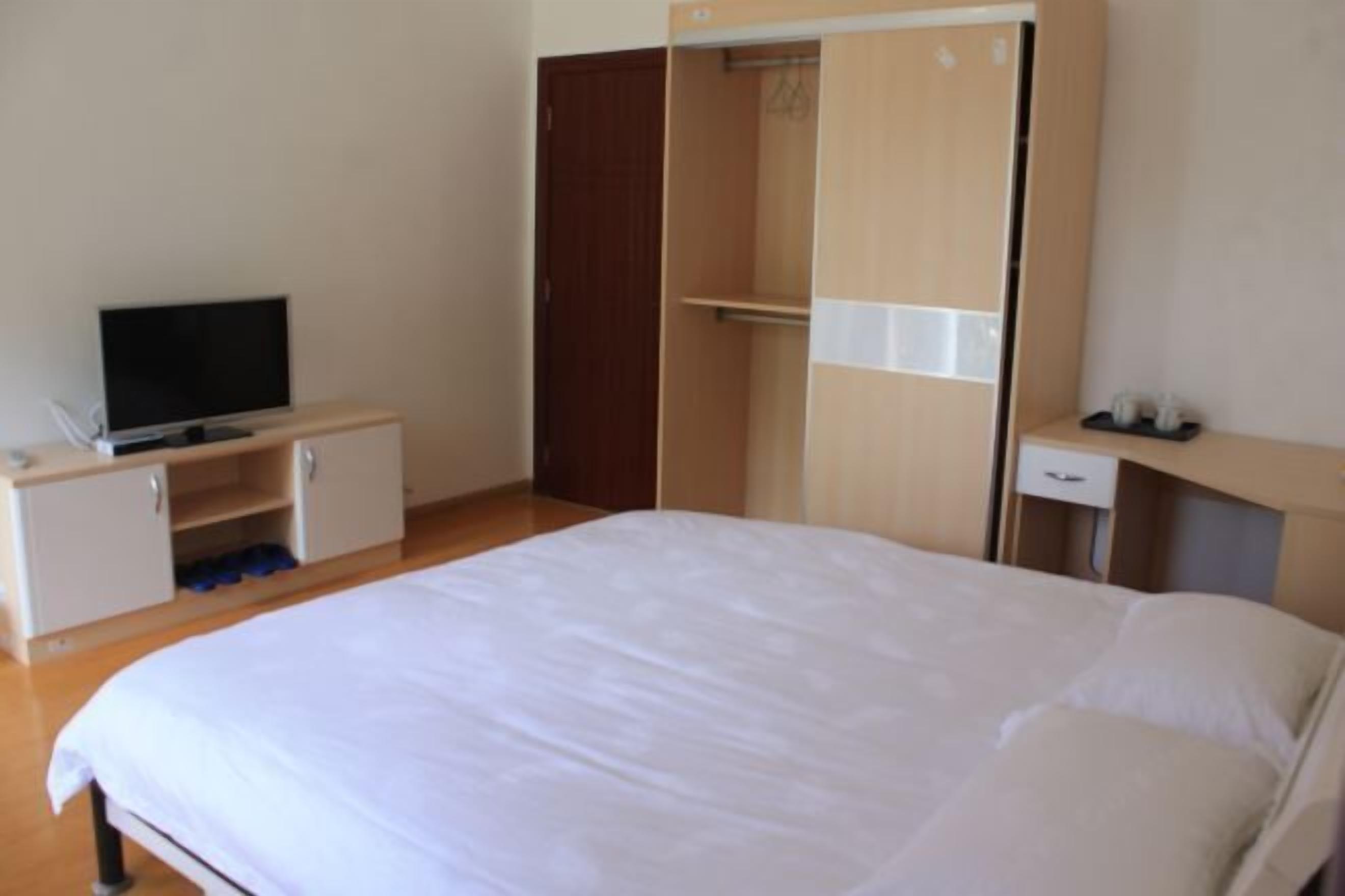 Ein Schlafzimmer mit einem Bett, einem Fernseher auf einem Schrank, einem Kleiderschrank und einem kleinen Schreibtisch mit Stuhl.