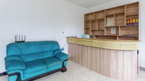 A reception area with a wooden counter and shelves, a teal sofa, and a small table. - Shanxing Inn (Zhangjiajie)
