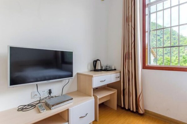 A room with a flat-screen TV, a desk with drawers, a kettle, and a window with curtains. - Shanxing Inn (Zhangjiajie)