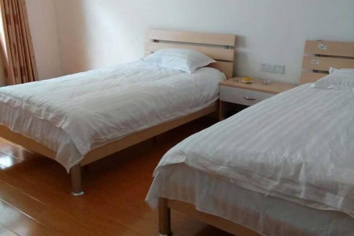 A hotel room with two single beds, wooden headboards, a bedside table with a lamp, and a small dresser.