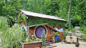 Una casa al estilo Hobbit con una puerta redonda, bancos de madera y plantas en macetas.