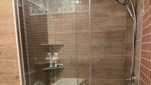 A glass-enclosed shower stall with a handheld showerhead, a glass door, and a towel rack on the wall.