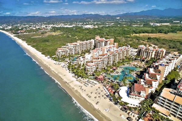 Resort costeiro com vários edifícios, frente mar e área de piscina central.