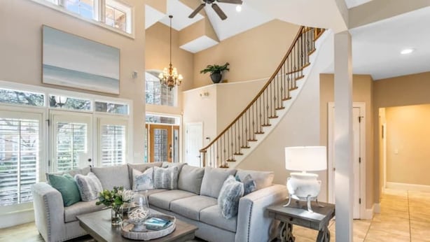 A spacious living room with a large sectional sofa, a wooden coffee table, a staircase, and a view through large windows.