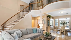 A spacious living area with a curved staircase, a gray sofa, a wooden coffee table, and a dining area with chairs and a table.
