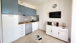 A modern kitchen with grey cabinets, a dishwasher, a microwave, and a small table with a remote control. - T2 walking distance from the beach - swimming pool & seaside getaway (Linguizzetta)