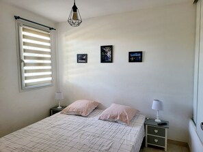Une chambre à coucher comprenant un lit, deux tables de chevet, une fenêtre avec des stores et trois tableaux encadrés accrochés au mur.
