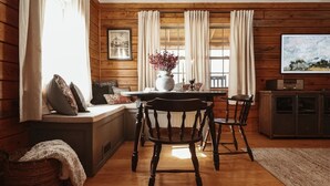 A cozy cabin-style room with a wooden interior, a dining table with chairs, a bench with cushions, a fireplace, and a television on a cabinet.