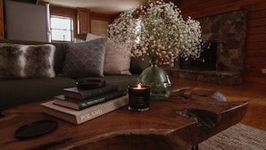 A cozy living room with a wooden coffee table, books, a candle, and a vase of flowers.