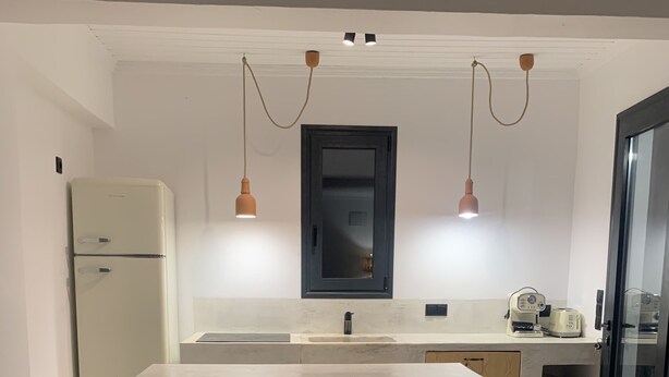 A modern kitchen with a central island, pendant lights, a built-in oven, and a refrigerator. - Porto Cheli, charming house with garden, 5 min. from beach and coves (Porto heli)
