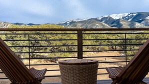 A balcony with two wooden chairs and a wicker table, overlooking a mountainous landscape.